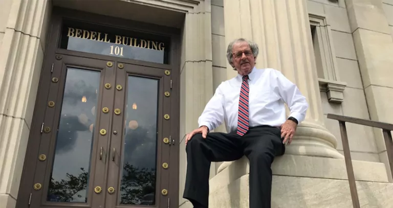 Hank Coxe sits against a podium outside of the Bedell Firm building