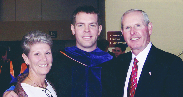 Brian Coughlin wears a graduation robe and poses with his parents