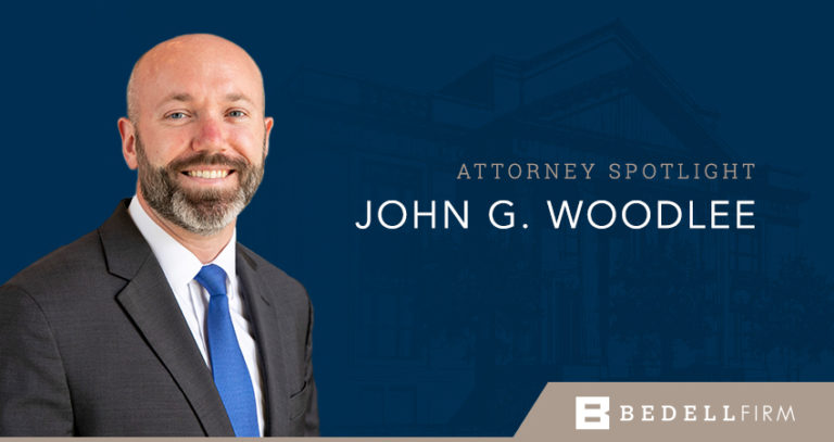 John Woodlee smiles against a blue background. Text to his right reads "Attorney Spotlight John G. Woodlee" the Bedell Firm logo is at the bottom